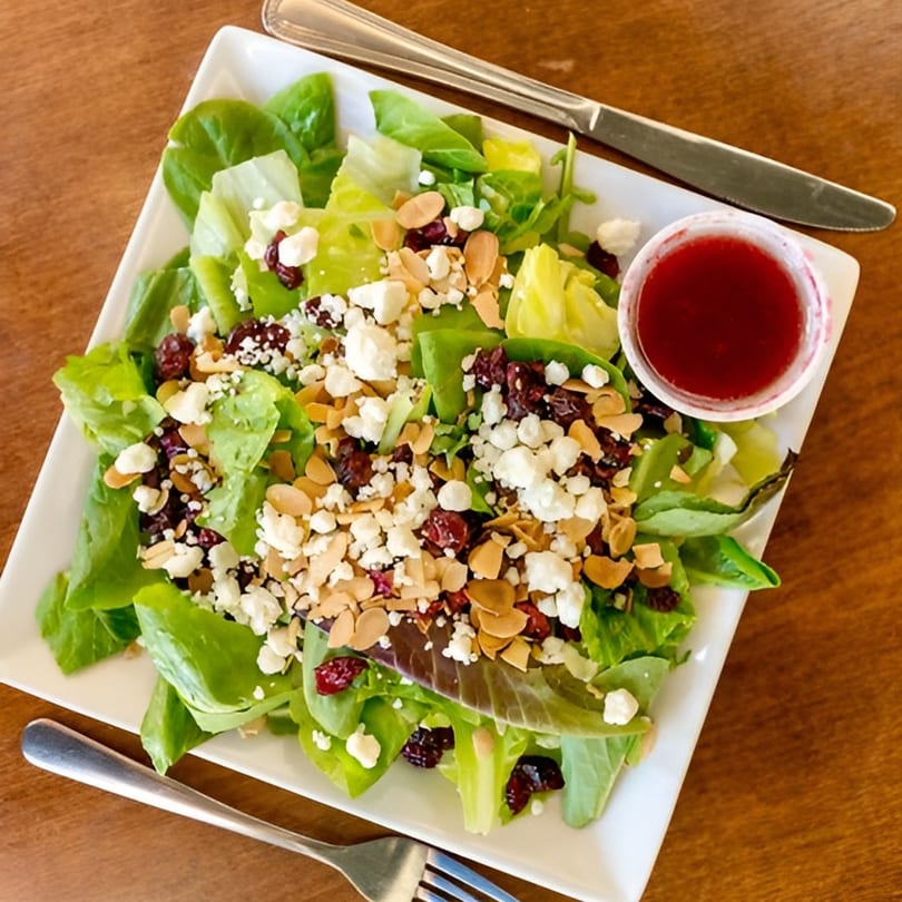 Fresh green salad with feta, dried cranberries, sliced almonds, and a side of raspberry vinaigrette.
